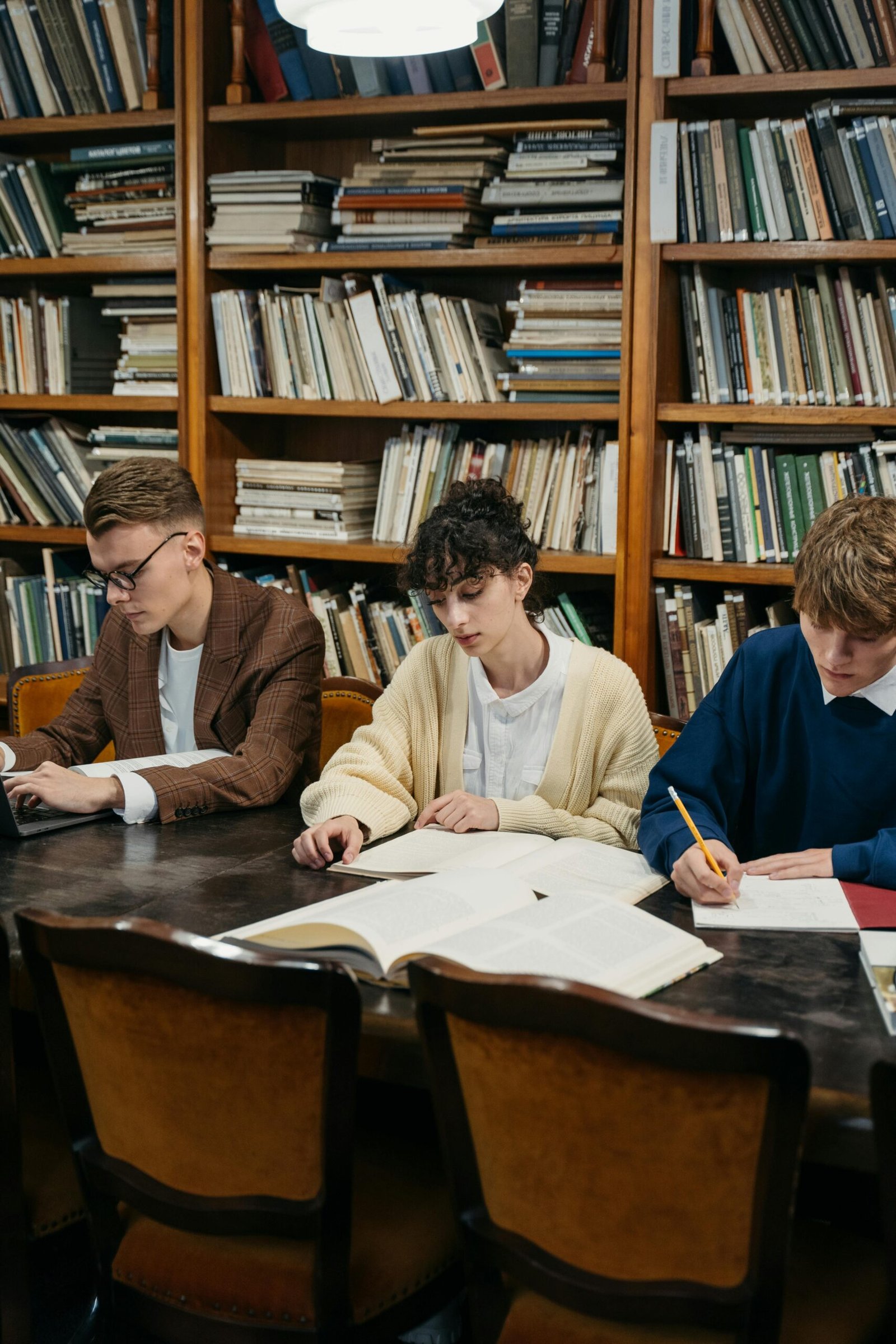 Students focused on studying in a university library filled with bookshelves.