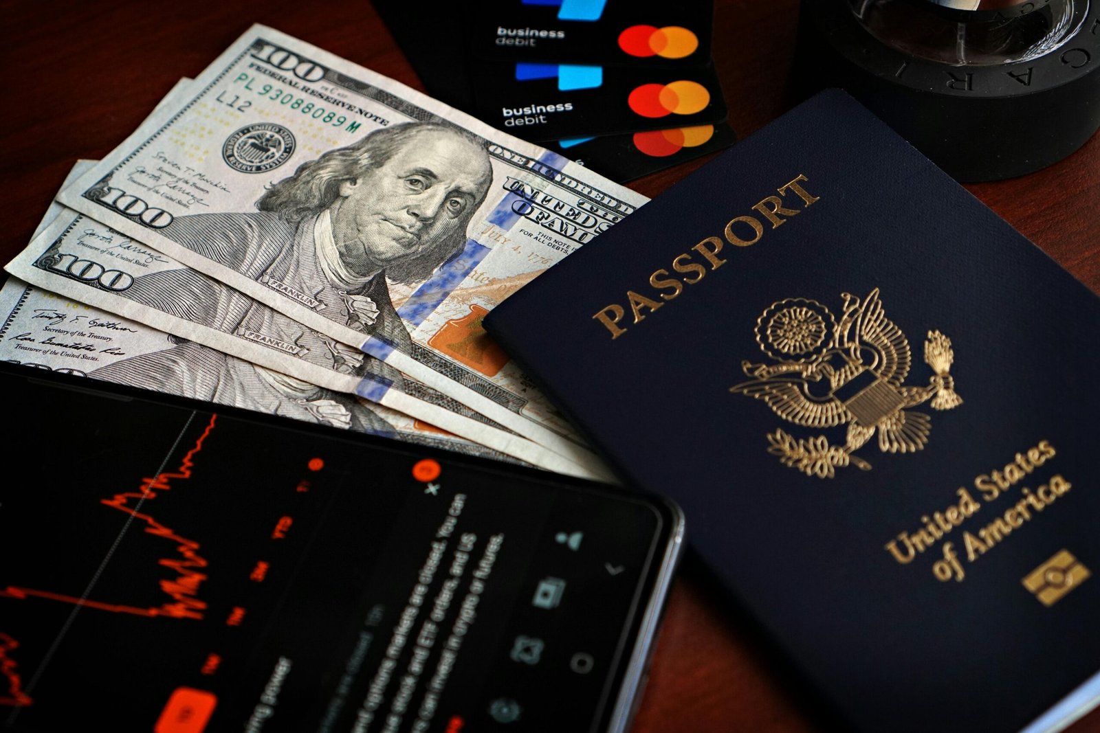 US passport with hundred-dollar bills, credit cards and smartphone showing stock data.